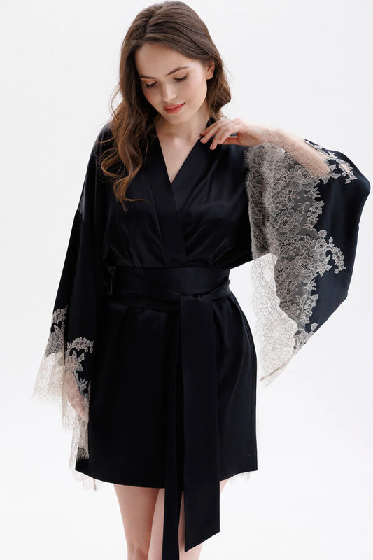 Woman wearing a black short silk robe with Leavers Lace sleeves showing the elegance of the sleaves. Long wide belt is completing the look.