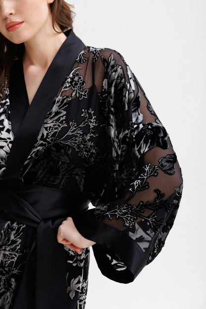 Woman wearing a black floral silk velvet kimono with wide belt. Front picture with accent on the sleaves. 