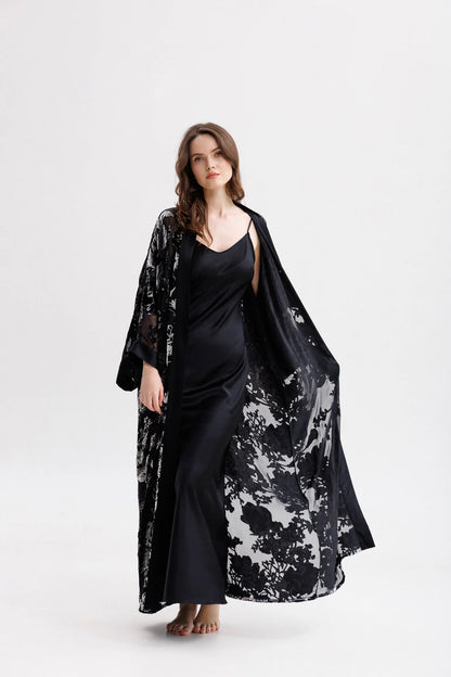 Woman wearing a long silk black slip dress on a spaghetti straps showing the front pose. She has a kimono in floral velvet and silk(sold separately) 